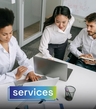 Three people in a business meeting at the office, reviewing information on their laptops. The word "services" is overlaid, representing professional services.