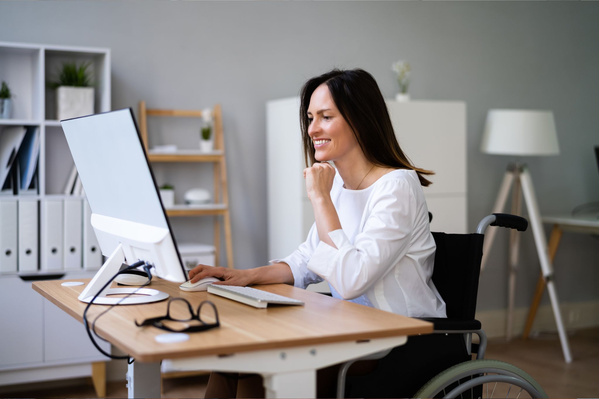 Una mujer con movilidad reducida, sentada sobre sociedad de ruedas, trabaja en su ordenador aprovechando las bondades de la inteligencia artificial y la accesibilidad digital.