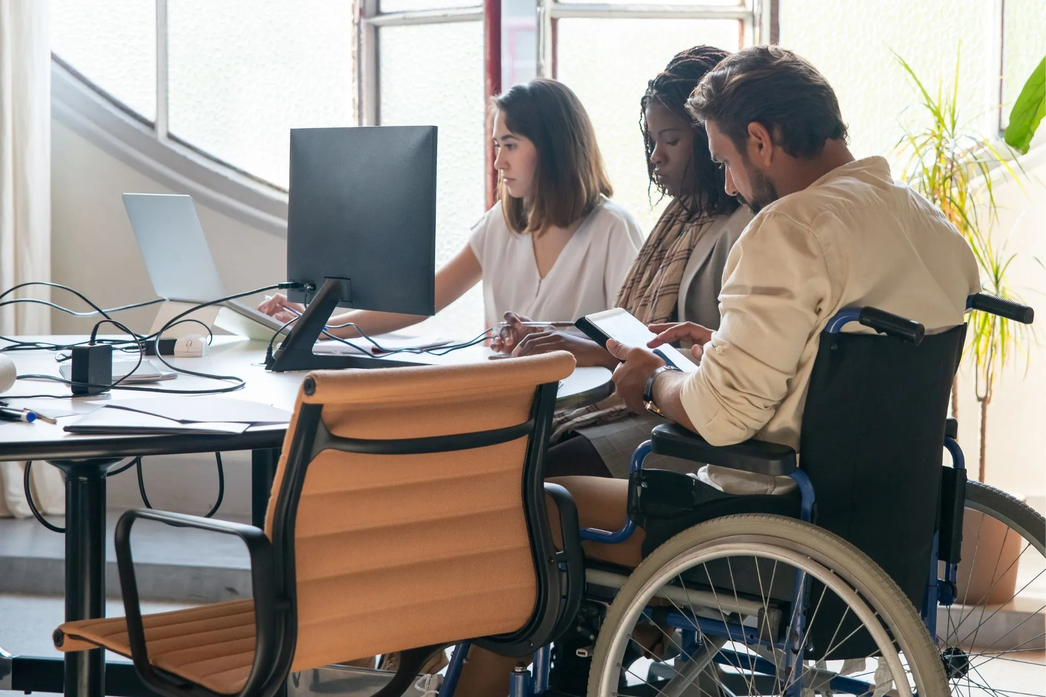 Un grupo de tres personas, una de ellas con movilidad reducida, analizan las pautas de accesibilidad para el contenido web 2025.